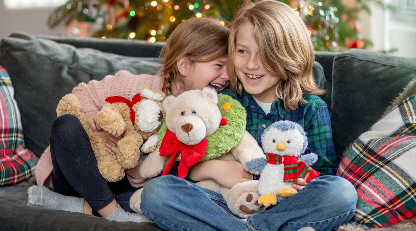 Two children sitting on a couch with stuffed animals, decorated room in the background