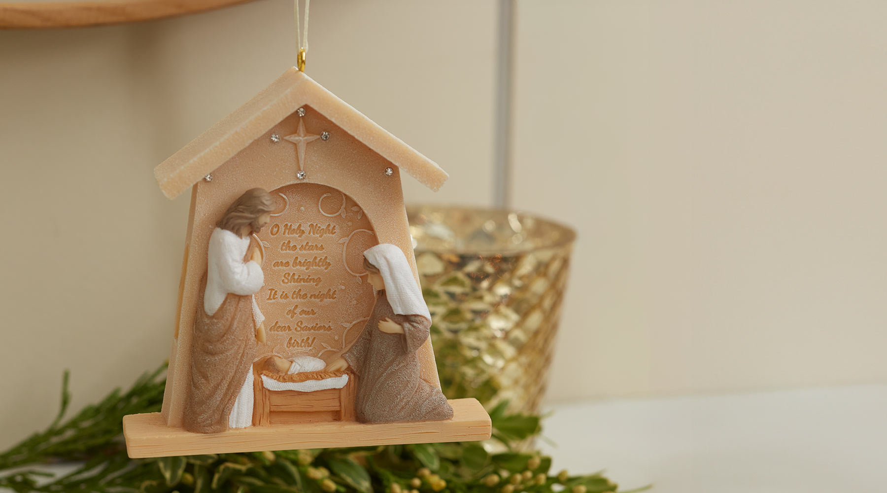 Decorative nativity scene ornament with two figures and a cross on a beige background.