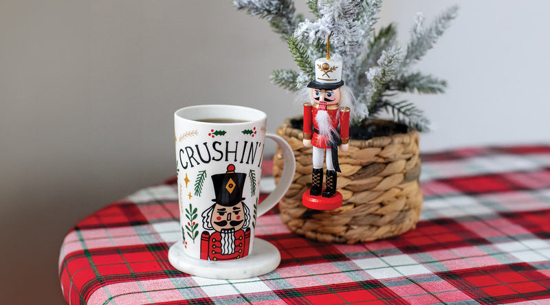 Mug with 'Crushing' design on a plaid tablecloth with a nutcracker and small tree.