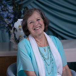Artist Sharon Thayer sitting in a chair with a floral arrangement in the background